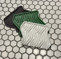 Three textured soap dishes in black, green, and white on a hexagonal tile pattern